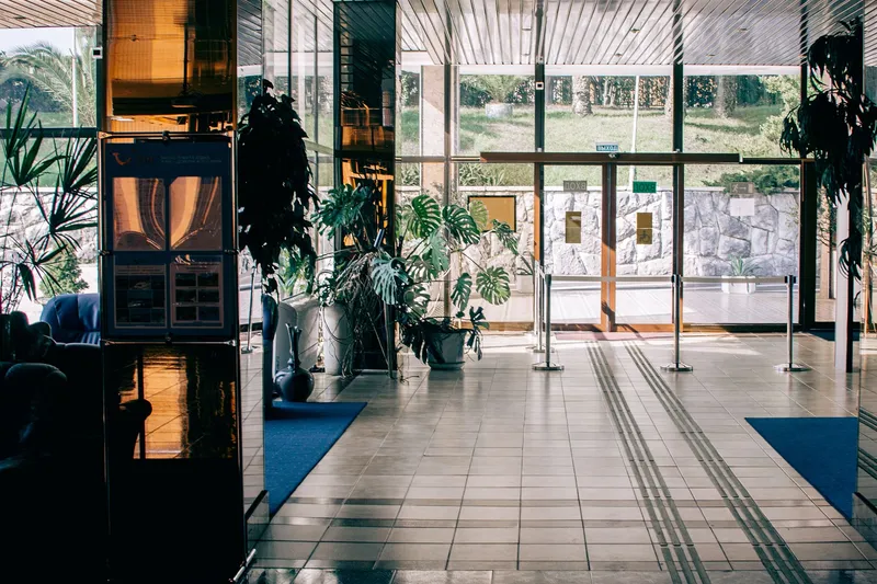 A light-filled building lobby with glass doors, large potted plants and a patterned tiled floor